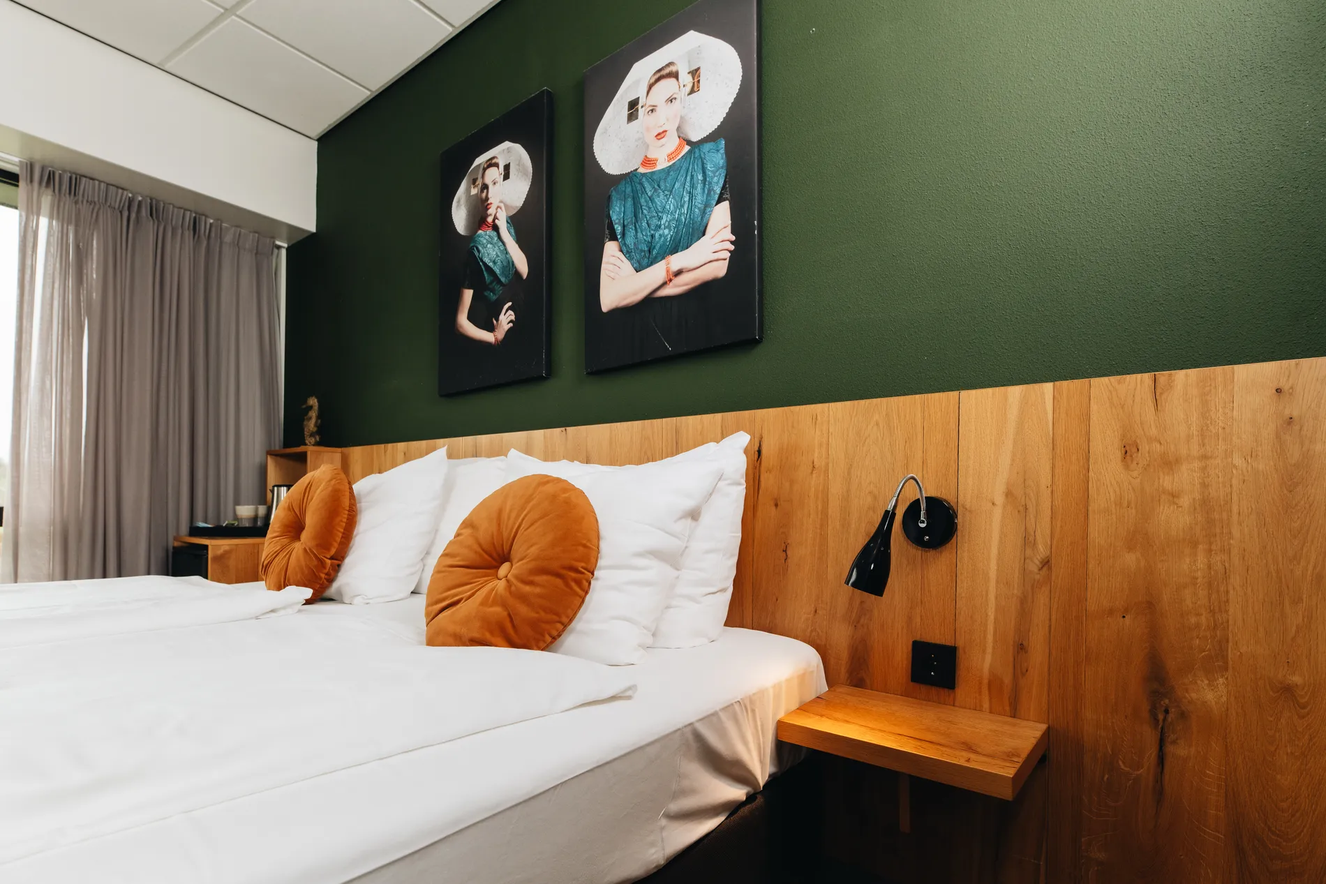 Luxe hotelbed met witte lakens en oranje sierkussens tegen een sfeervolle donkergroene wand met moderne kunst in Resort Land & Zee.